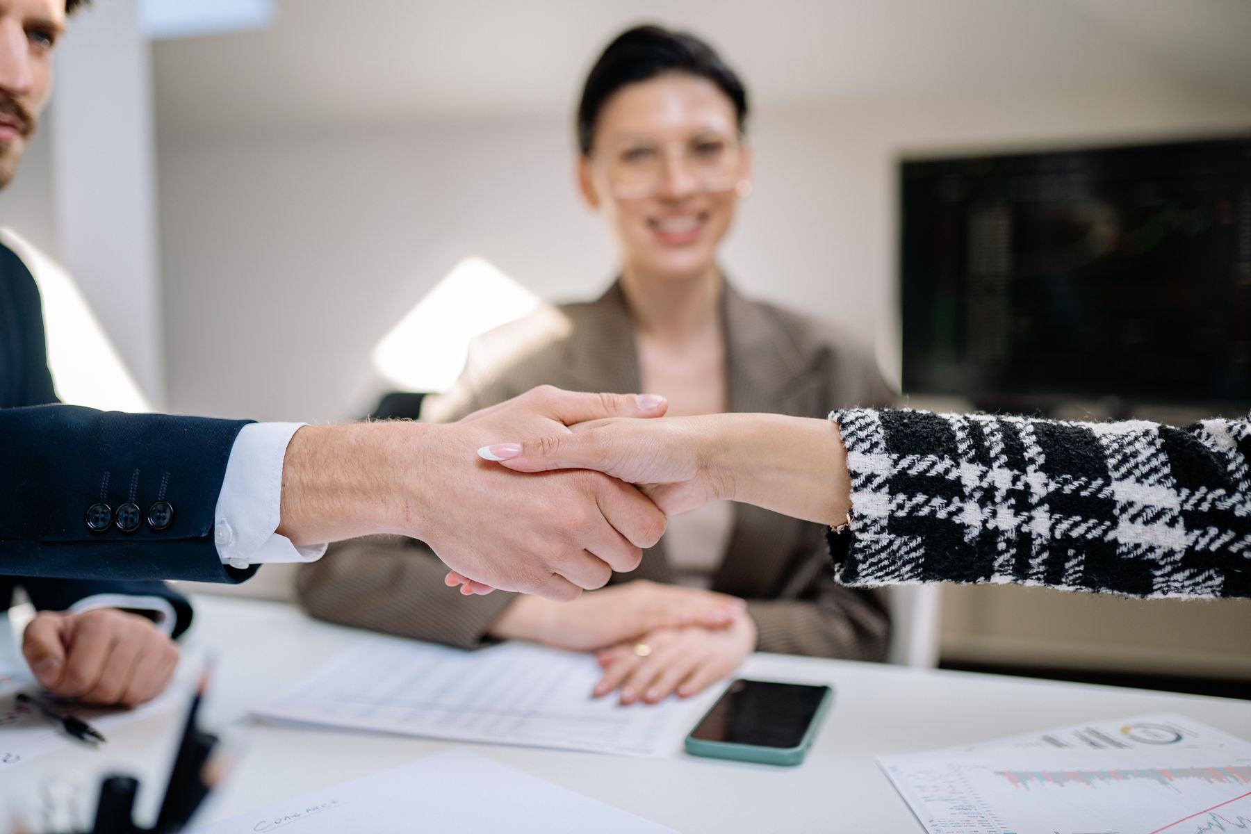 Reunião de negócios com aperto de mão e executiva sorrindo ao fundo